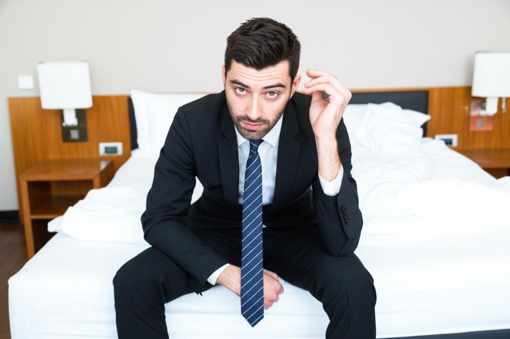 tired sales man sitting on hotel bed looking stressed