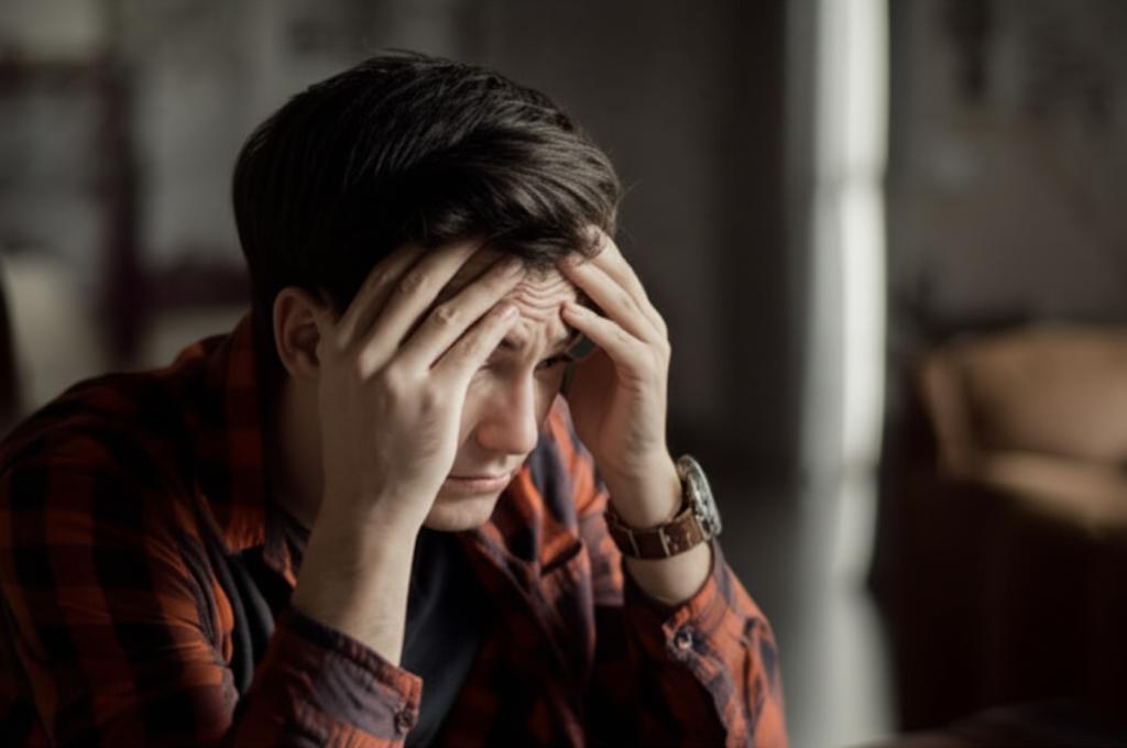 Man looking stressed and insecure, sitting alone with head in hands, dark lighting